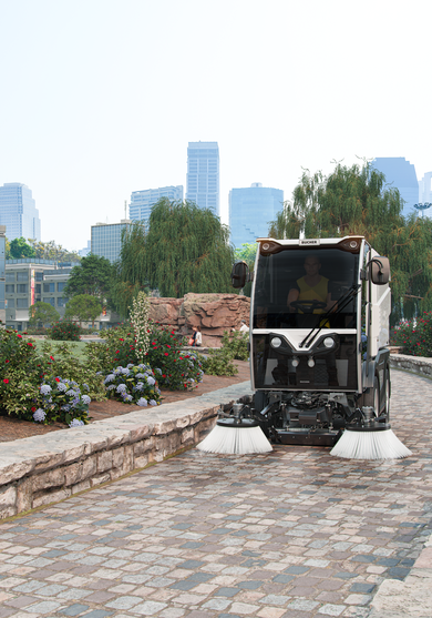 Eine CityCat VR17e Kehrmaschine von Bucher kehrt einen Gehweg in einem Park.